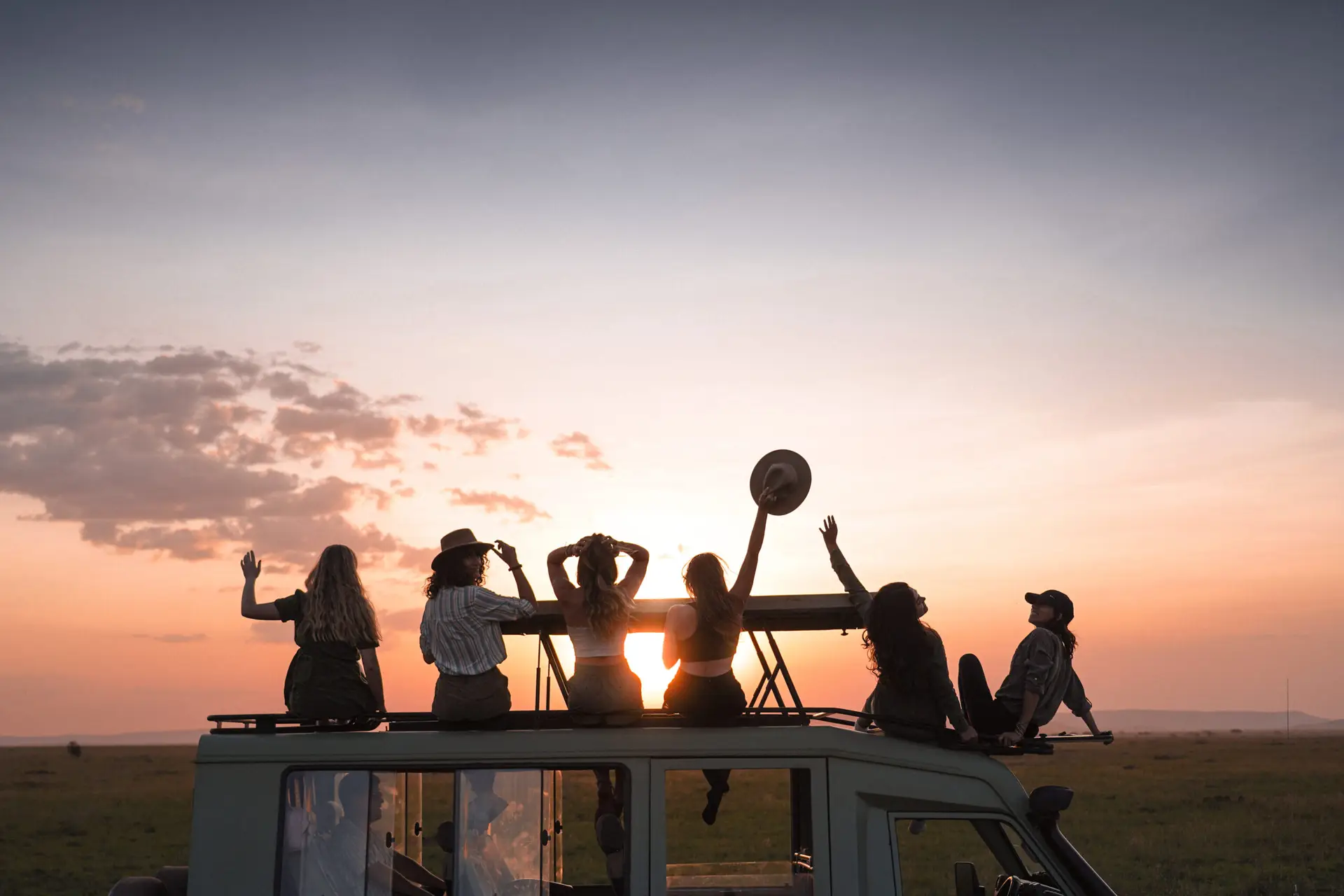 Women silhouetted against a golden sunset while sitting on the roof of a safari vehicle on the savanna